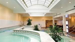 Indoor spa pool with arched skylight, cream walls, tiled edges, and green plants.