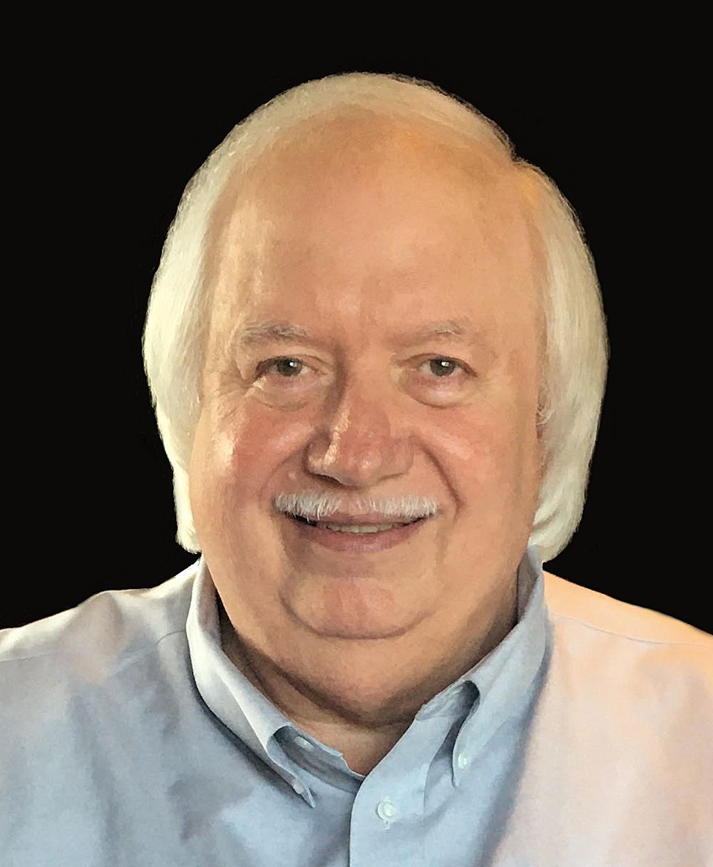 Man with white hair, mustache, smiling, wearing a blue shirt.
