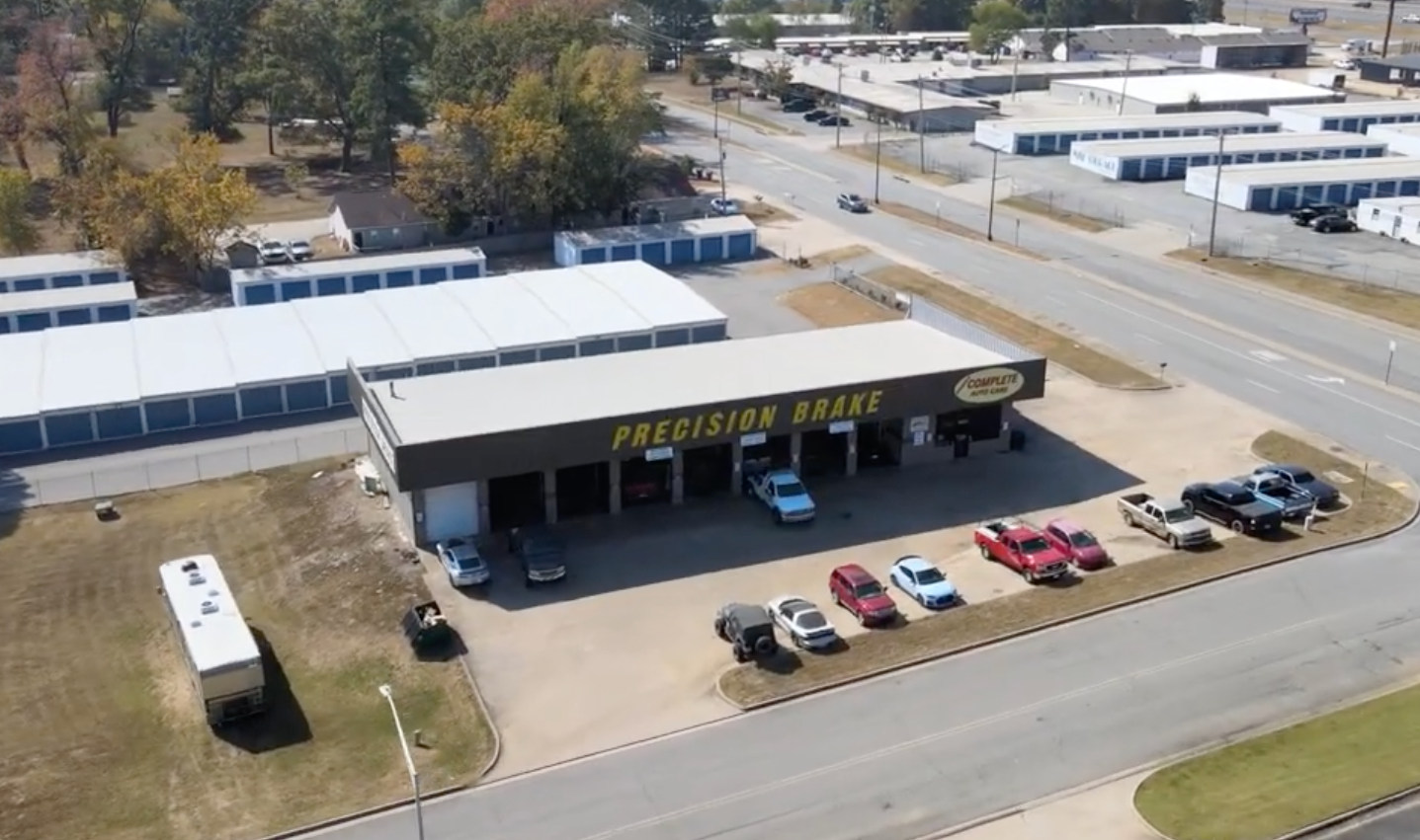 Aerial view of Precision Tune auto shop with cars parked outside, storage units and a road visible.