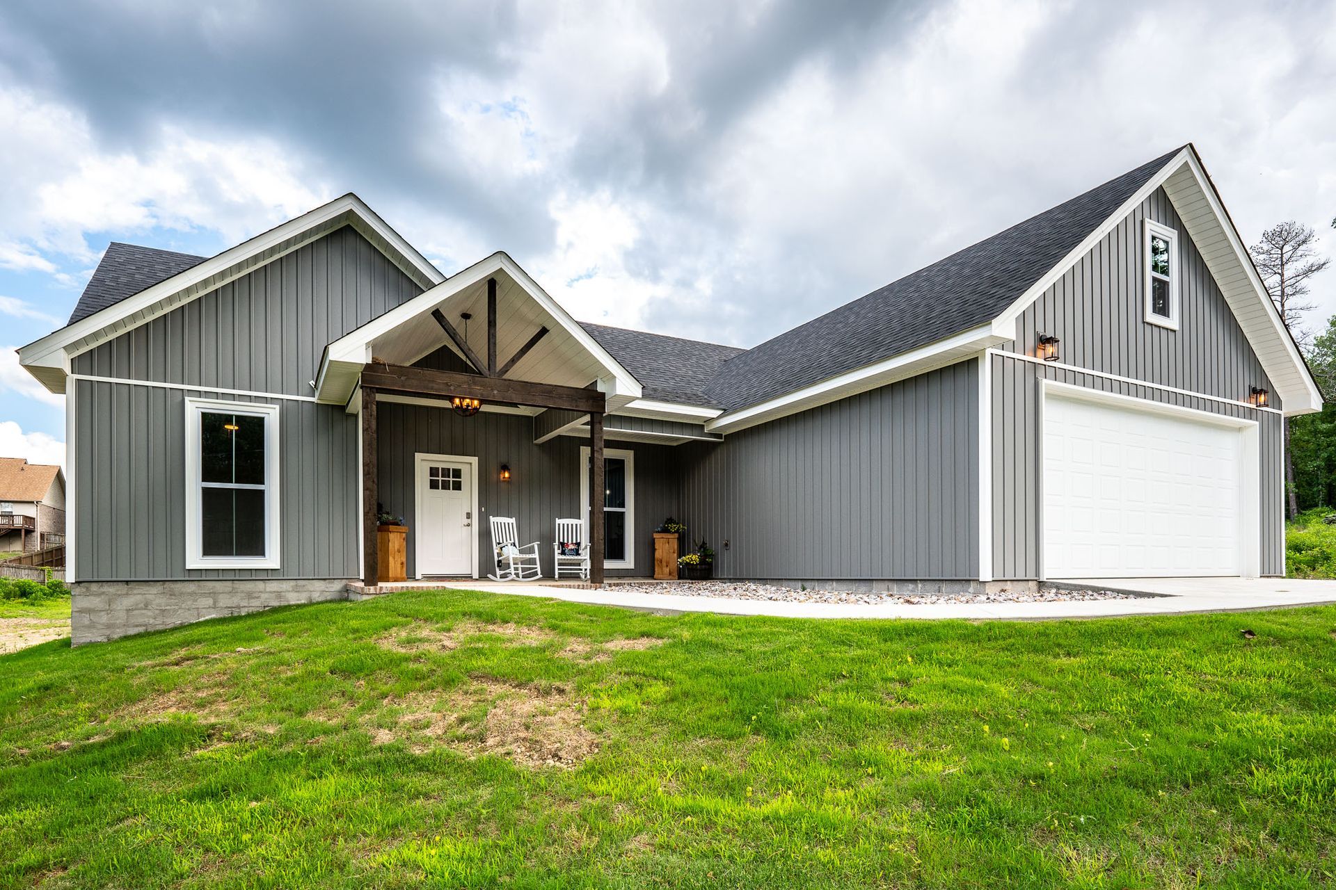 Gray farmhouse with white trim, garage, and front porch under cloudy sky.