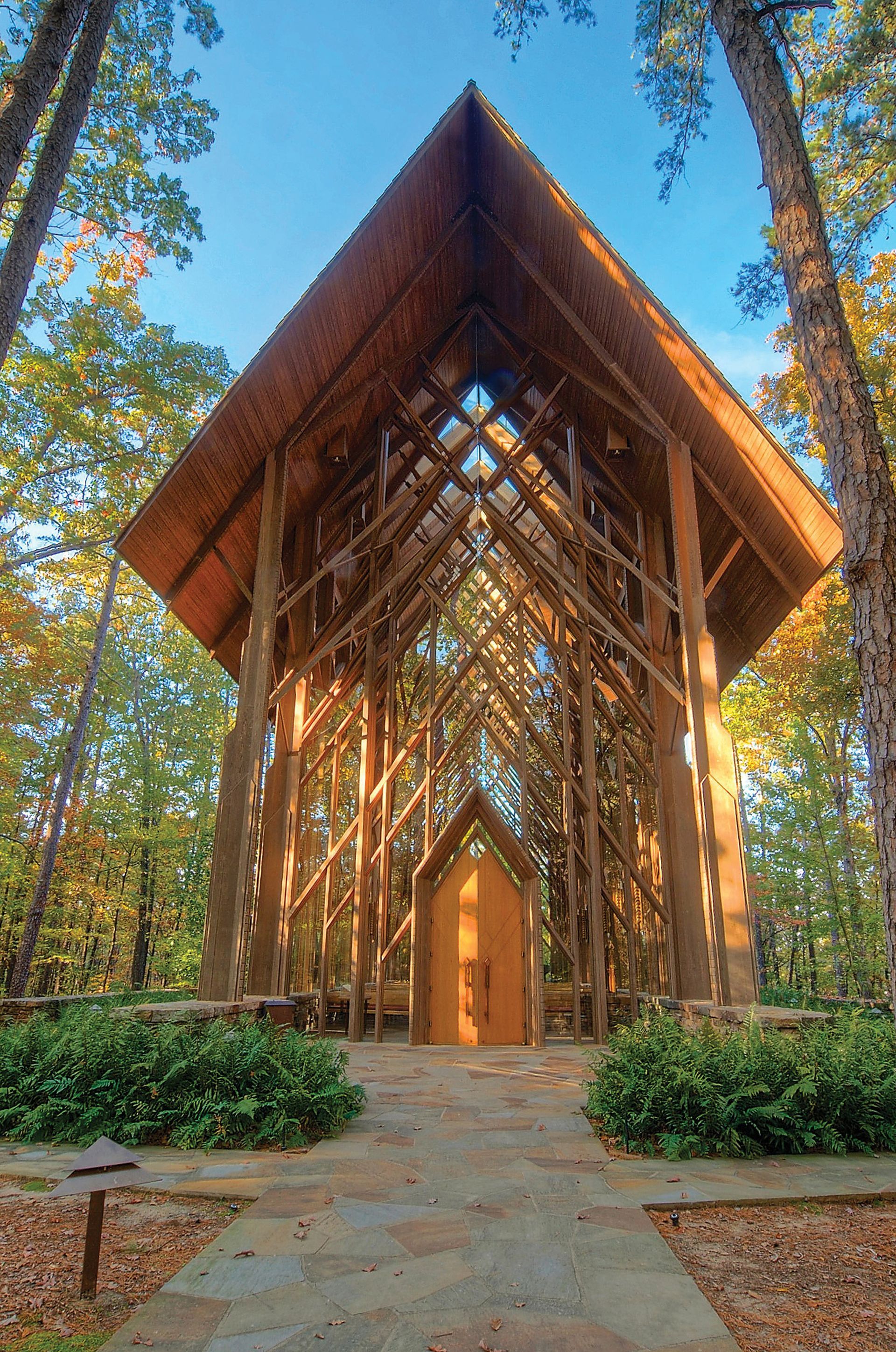 Open-air wooden chapel with an angular roof in a forest setting.