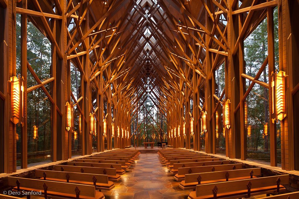 Wooden church interior with rows of pews, arching beams, and side lights, set in a forest.