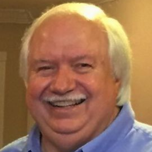 Smiling older white man with white hair wearing a blue shirt.