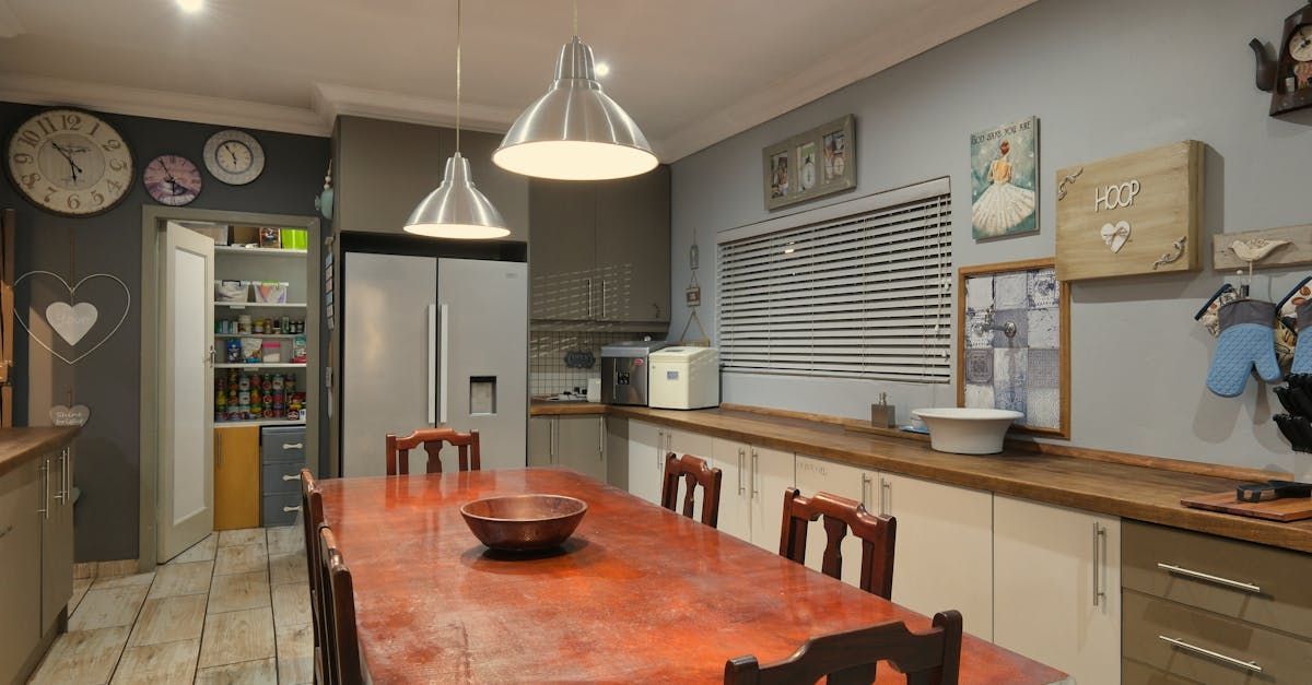 Kitchen with long wooden table, cabinets, refrigerator, and hanging pendant lights.