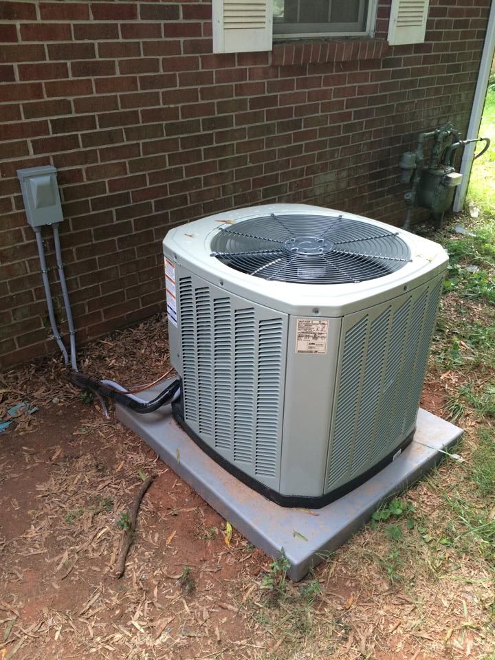 An outdoor HVAC unit sitting on a concrete pad next to a red brick house wall.