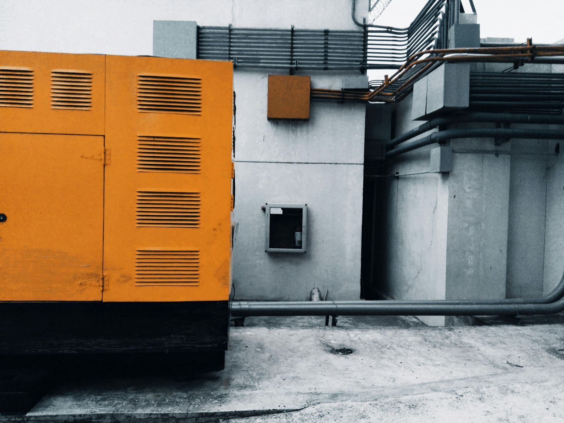 A vertical, galvanized steel HVAC ventilation duct mounted on the exterior white wall of a building.