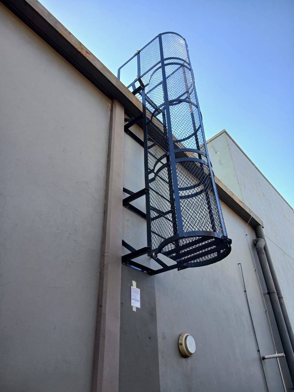 Black vertical caged ladder attached to a beige building exterior.