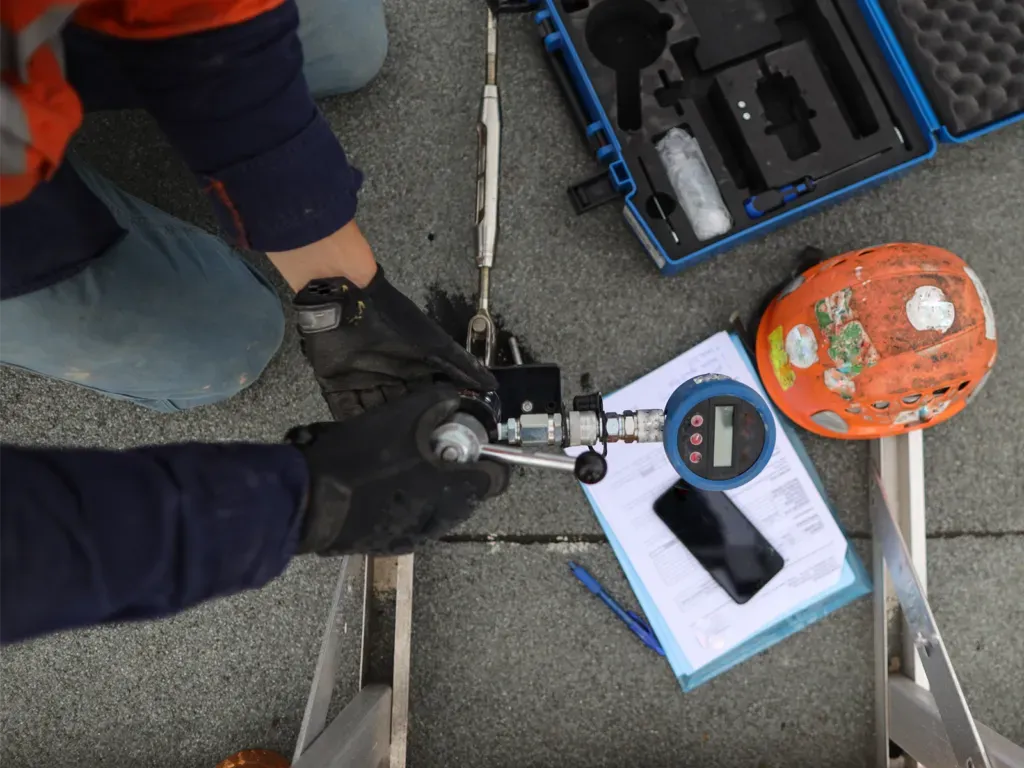 Person using a testing device on a roof with a digital gauge and paperwork.