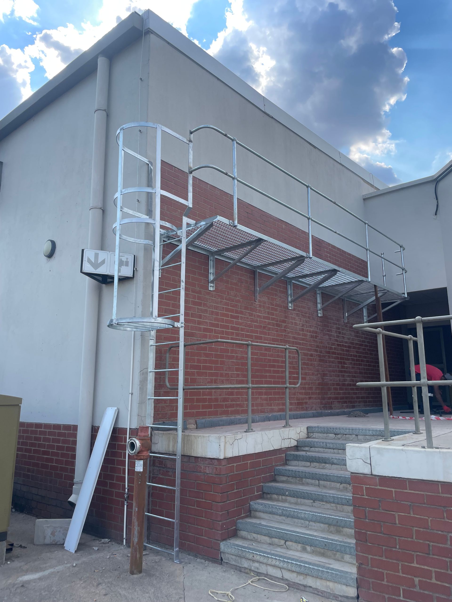 Exterior building with brick and white walls. Metal ladder and walkway alongside stairs. Cloudy sky.