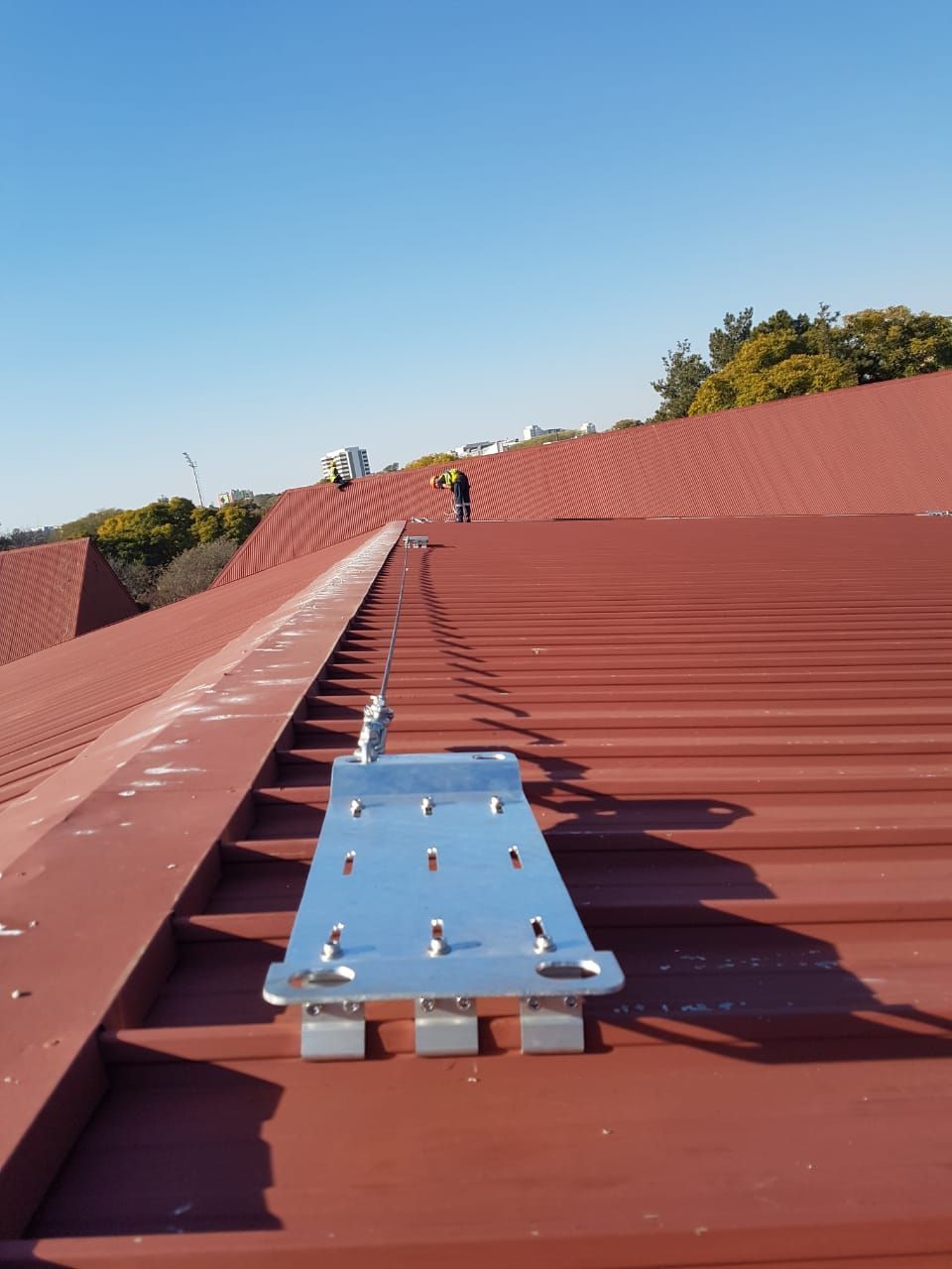 Metal roof with installed safety rail, workers on roof, blue sky.