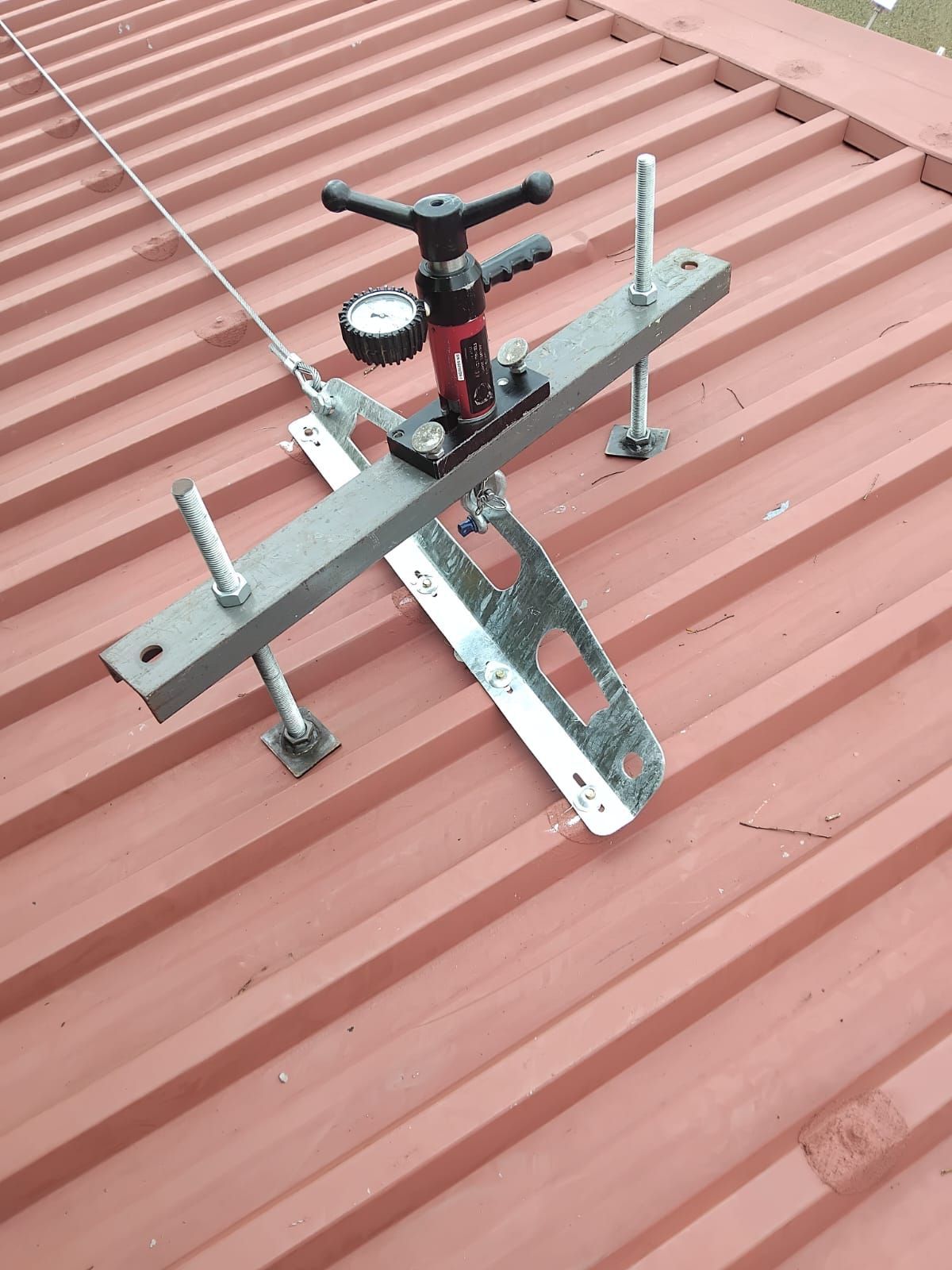 Gloved hands use a tool on a roof. A clipboard and scaffolding are in the blurry background.