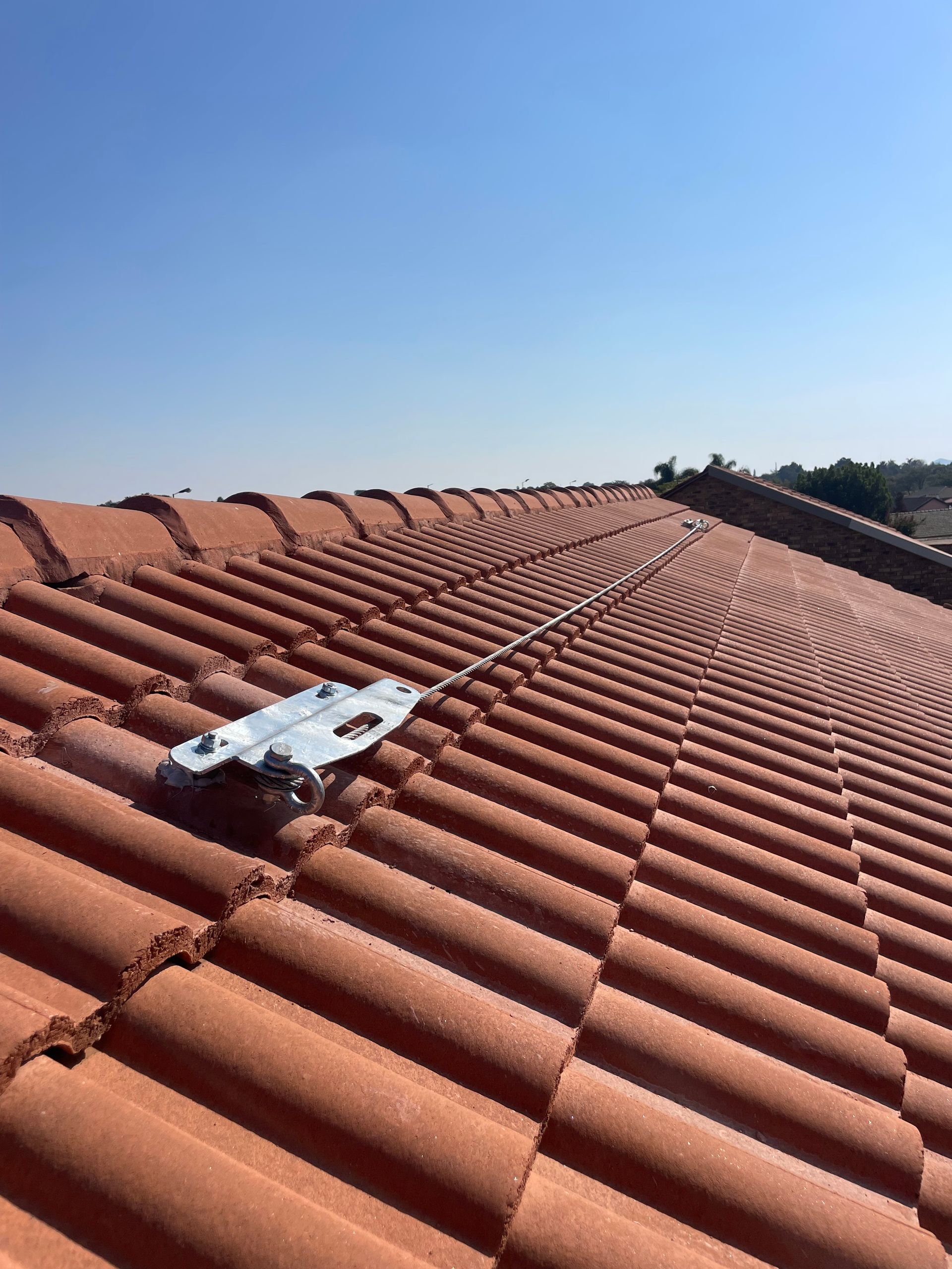 Rooftop with orange clay tiles, fall protection device laid out, clear blue sky.