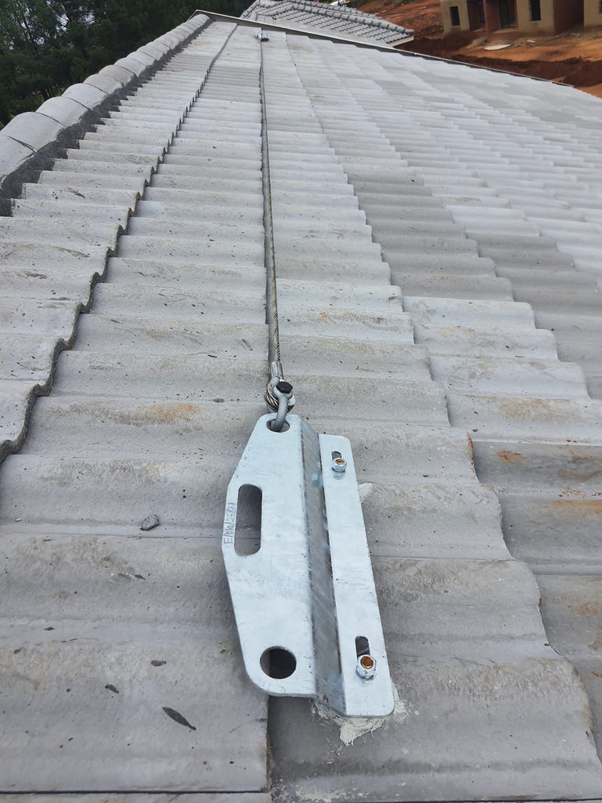 A metal safety device with a cable is secured to a tiled roof, likely for fall protection.