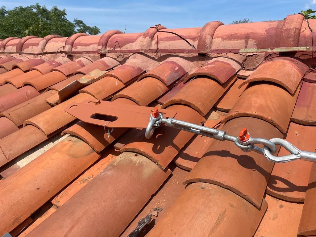 Metal roof safety anchor on red tile roof.