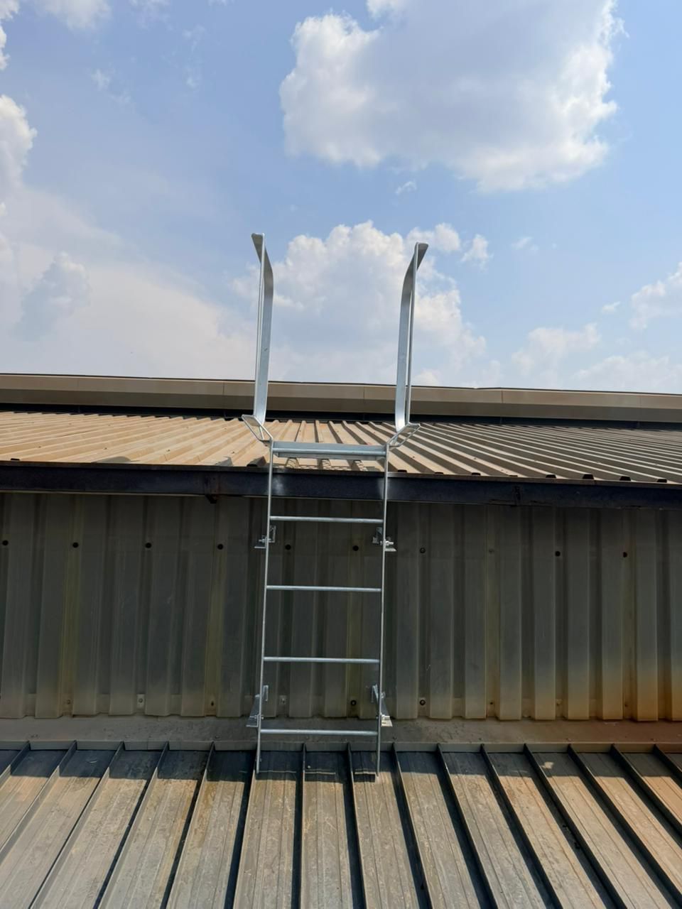Ladder leading up to a corrugated metal roof against a partly cloudy sky.