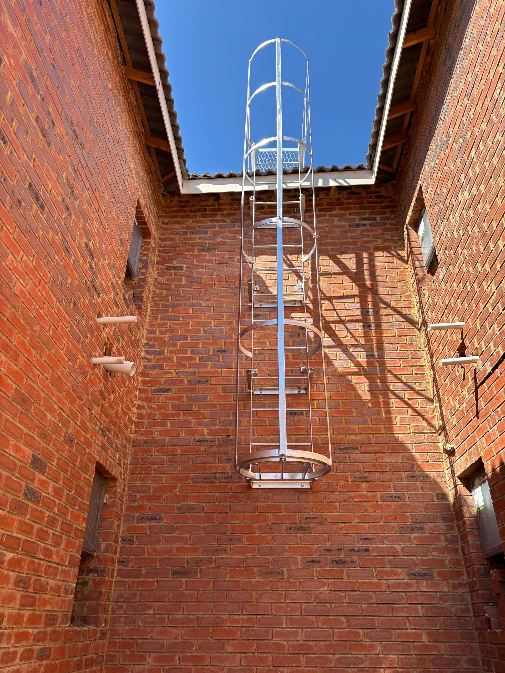 Metal ladder with safety cage attached to a brick building; blue sky overhead.