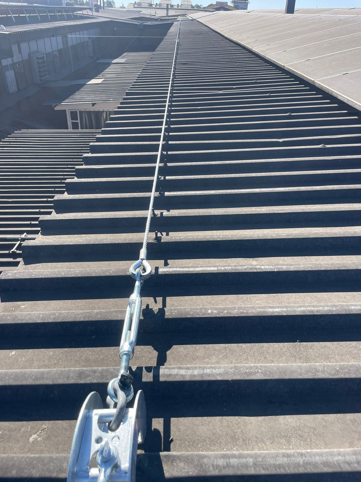 A safety lifeline stretches across a corrugated metal roof. Hardware and cables are visible.