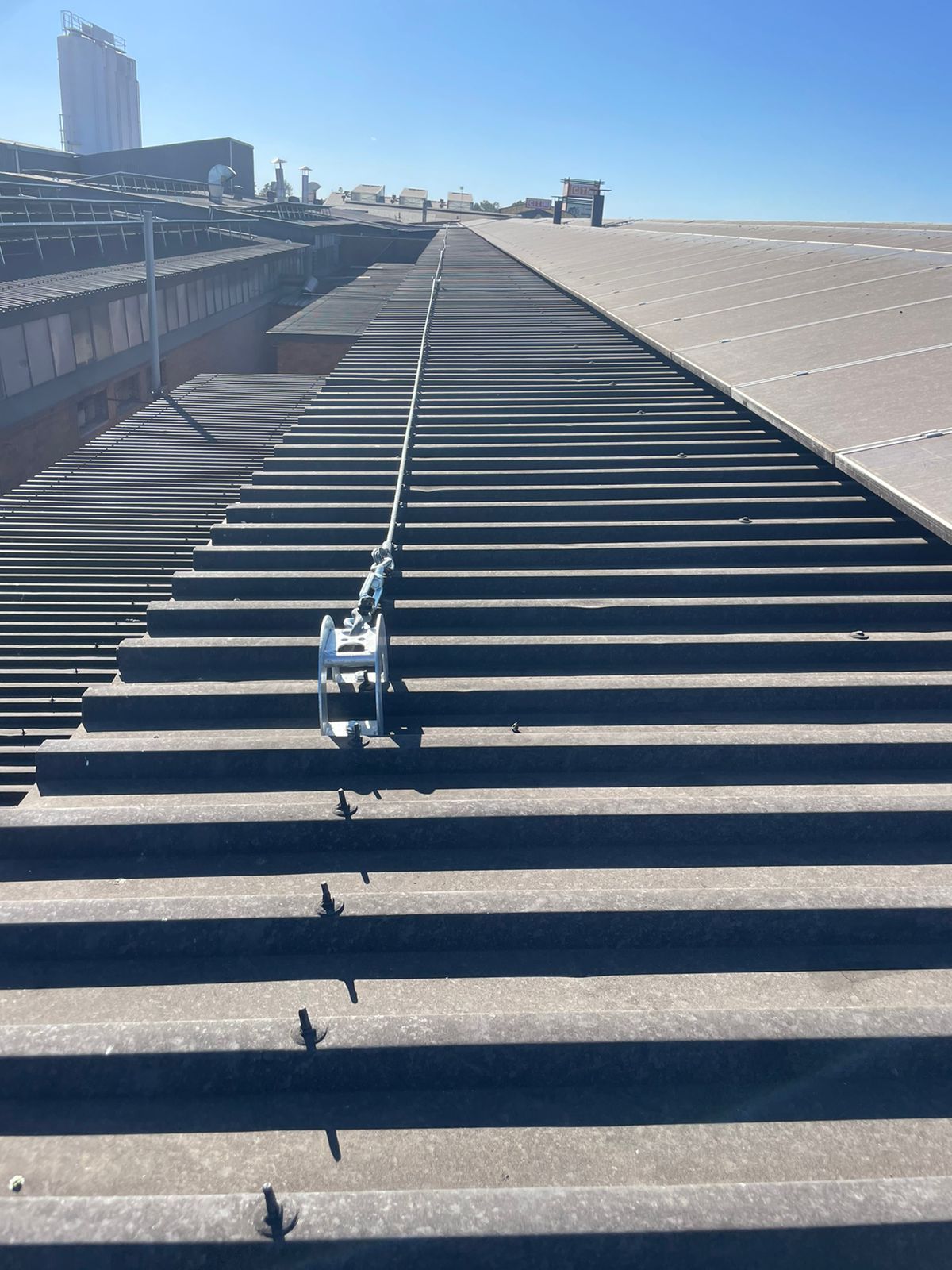 Rooftop with safety lifeline system installed. Gray corrugated roofing, blue sky.