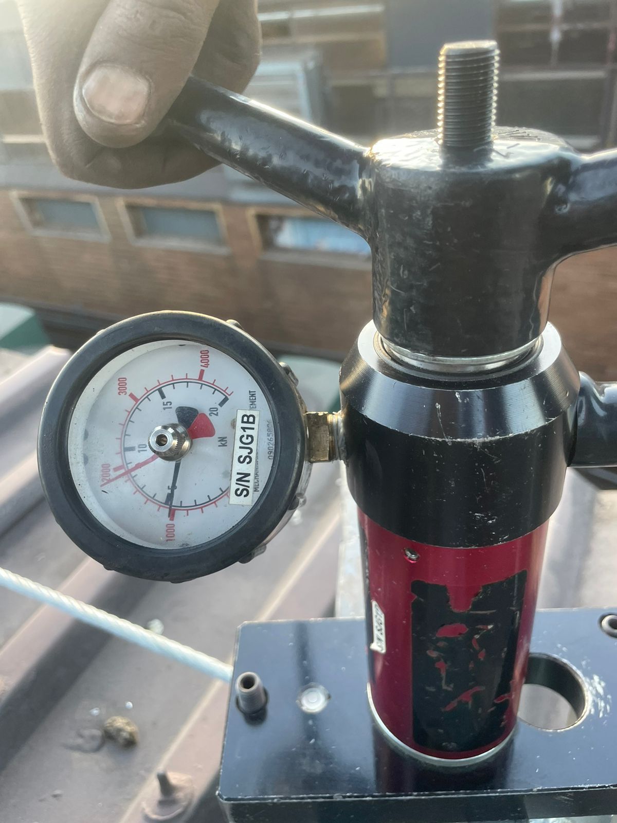 Hand turning a gauge on a red and black cylinder. The gauge reads pressure in a white-faced dial.