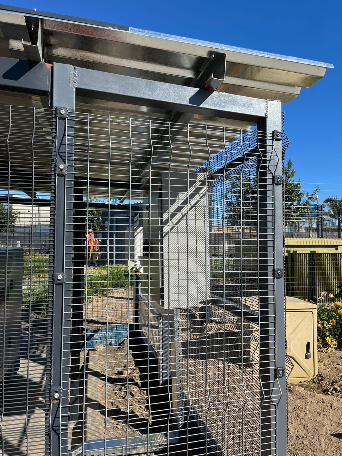 Metal cat enclosure with wire mesh walls and roof, outdoors.