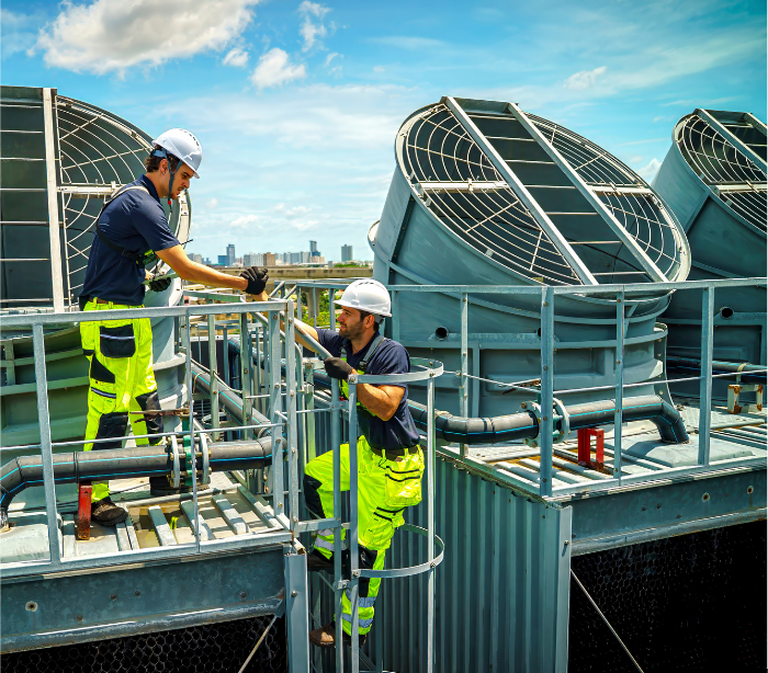 Two workers in safety gear inspect cooling towers on a rooftop.