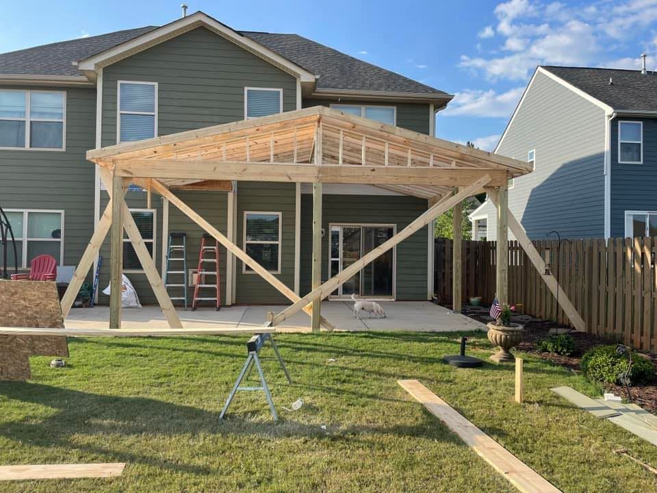 Backyard with a wooden pergola under construction, green grass, two-story house, sunny day.