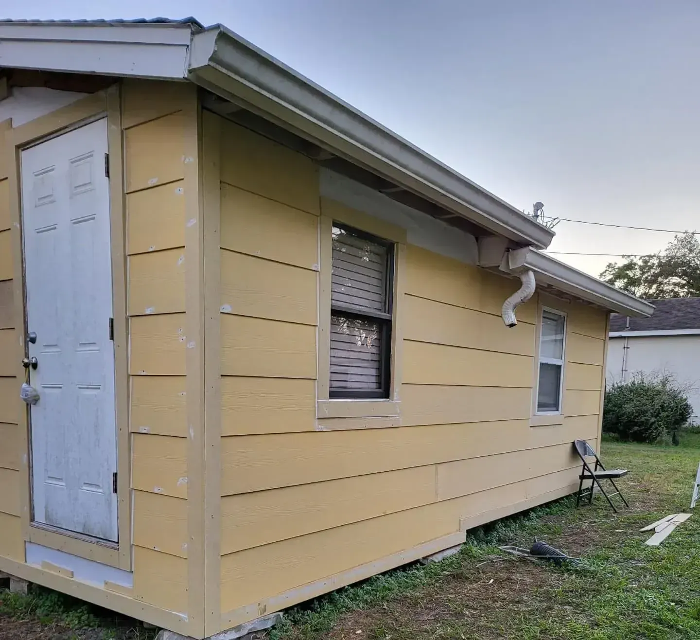 Backyard with a wooden pergola under construction, green grass, two-story house, sunny day.
