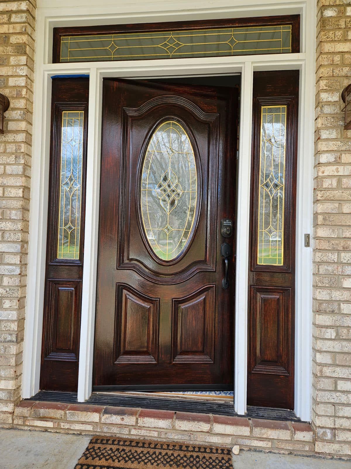 Brown stained wood front door with sidelights, transom window, and white trim.