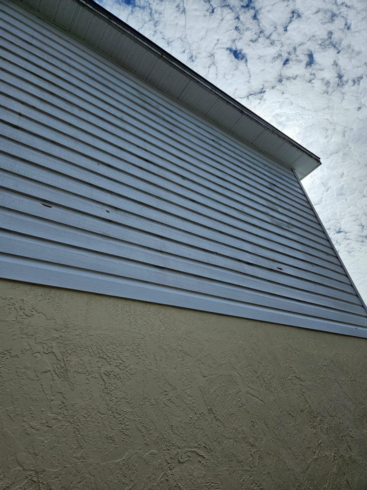 White stucco building with windows and palm tree against a bright blue sky. A sidewalk and greenery in the foreground.