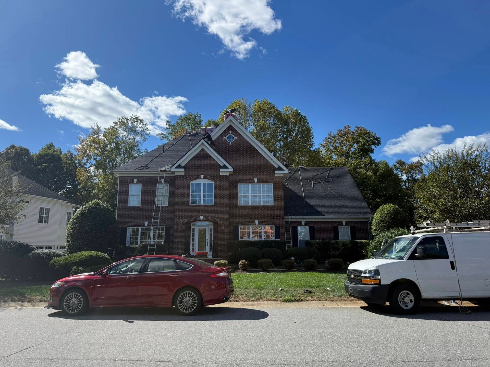 Brown house with red car and white van parked on the street on a sunny day.