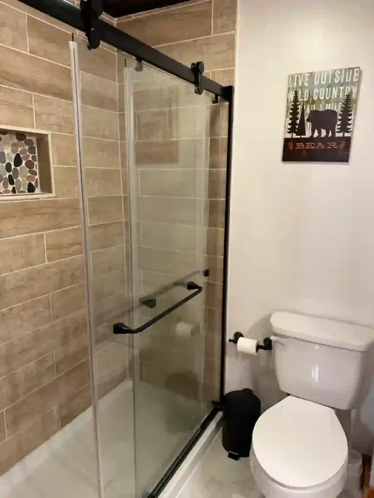 Bathroom with tiled walls, glass shower door, and toilet. A bear sign hangs on the wall.