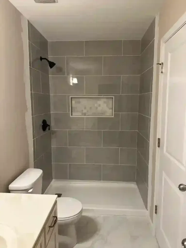 Bathroom with gray tiled shower, black fixtures, and white toilet.