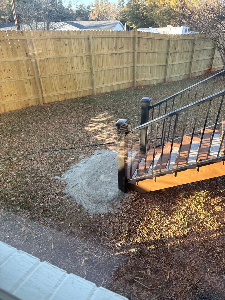 A wooden fence borders a yard with a wooden deck and stairs.  A pile of light-colored material sits near the stairs.