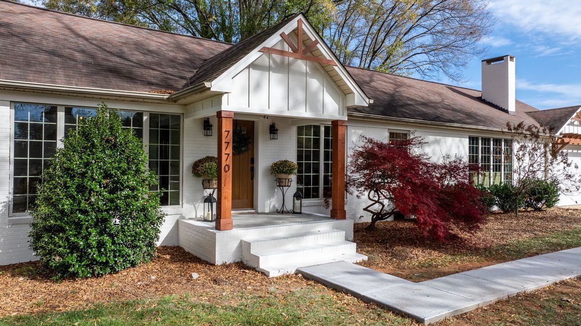 White-painted house with brown trim and steps leading to the front door, with fall foliage in front.