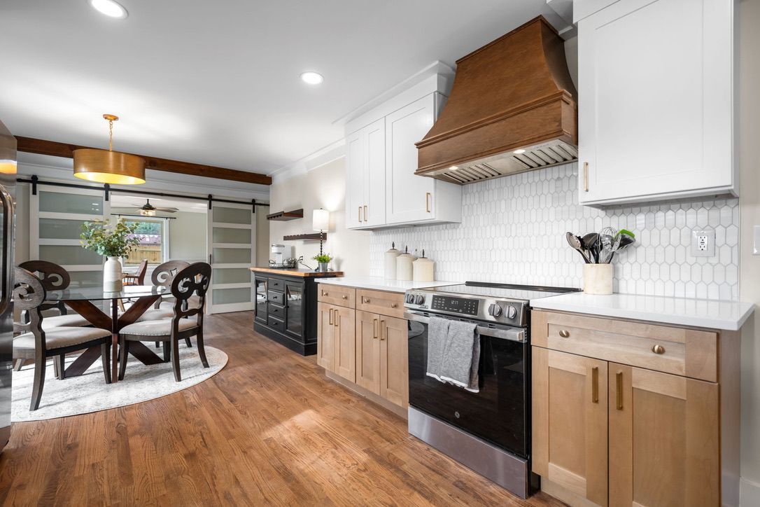 Modern kitchen with white and natural wood cabinets, stainless steel appliances, and a dining area.