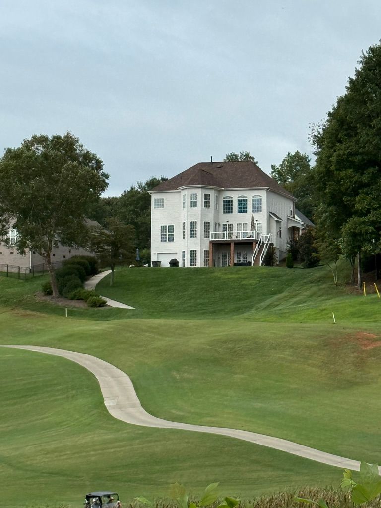 A white house on a green hill overlooking a golf course with a winding path and trees.