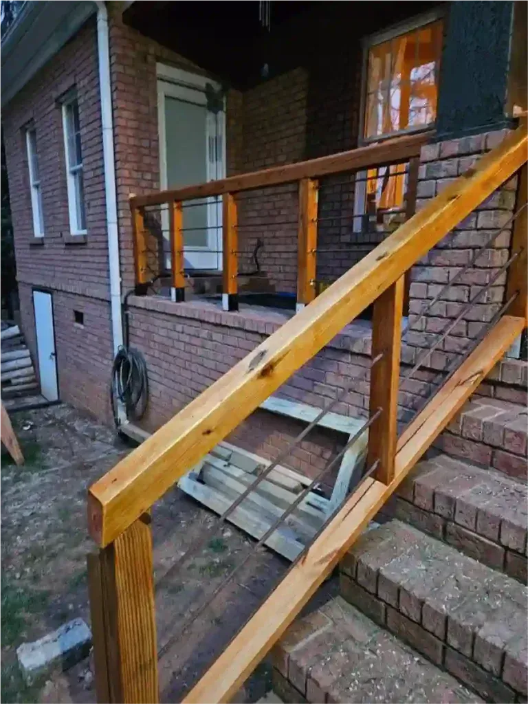 Wooden railing with cable wires on brick steps leading to a brick home's front door.