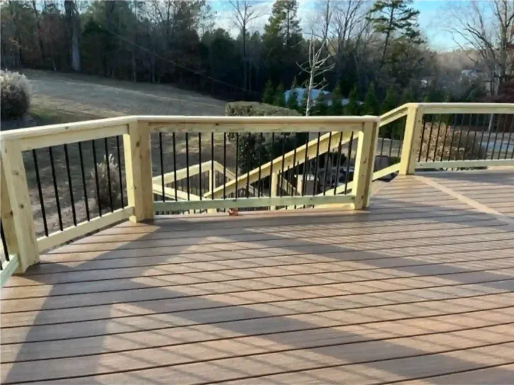 Wooden deck with light-colored railing and black metal spindles overlooking a grassy yard and trees.