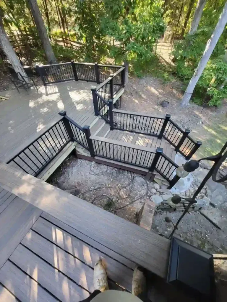 Multi-level wooden deck with black railings and steps leading to a lower level with a stone ground area.