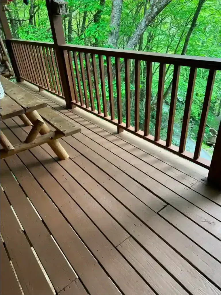 Wooden deck with brown railing, picnic table, overlooking a forest.