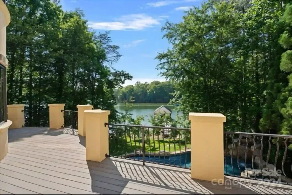 Deck overlooking a lake framed by trees, featuring light pillars and a wrought iron railing.