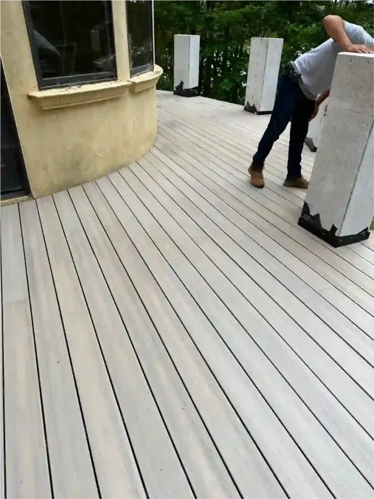 Person working on light-colored wooden deck with architectural columns. Curved edge of a building visible.