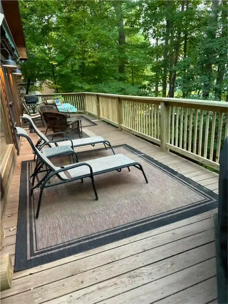 Wooden deck with lounge chairs and area rug, surrounded by trees.