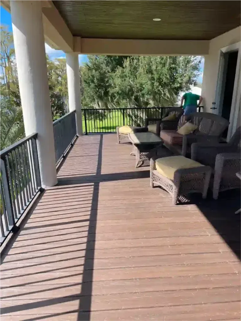 Covered outdoor patio with dark wood flooring, seating, and a view of trees.