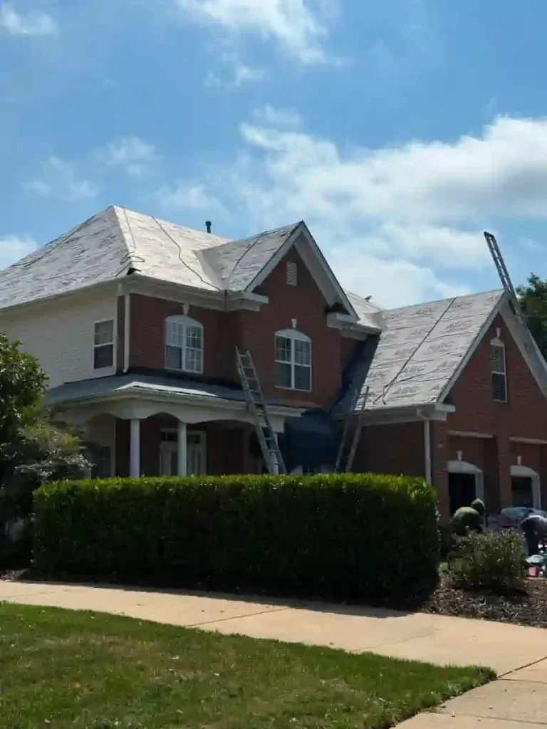 House with new roof partially installed, ladders against the side, workers in view.