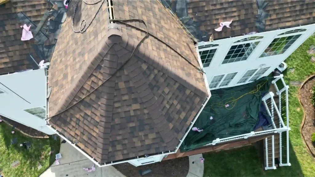 Overhead view of a house with brown shingle roof, green tarp covering patio, and white trim.