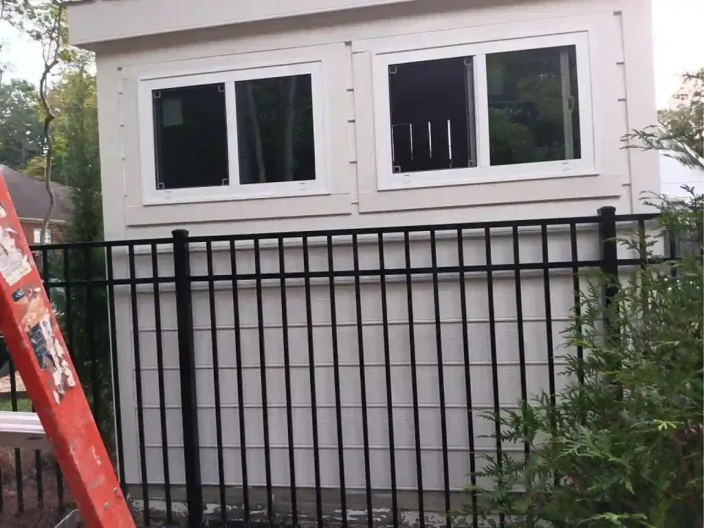 White building with two windows above a black fence. An orange ladder is on the left.