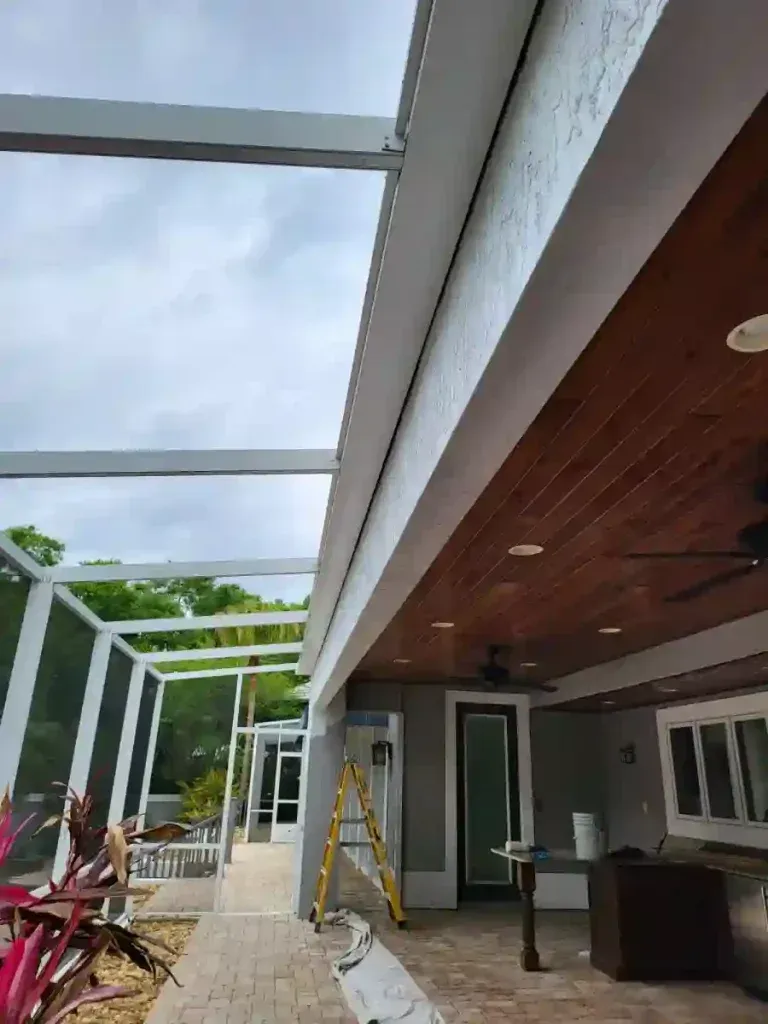 Patio with screen enclosure, white beams, wood ceiling, gray walls, ladder, and overcast sky.