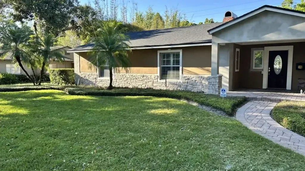 House with stone facade and walkway, surrounded by green grass and landscaping on a sunny day.
