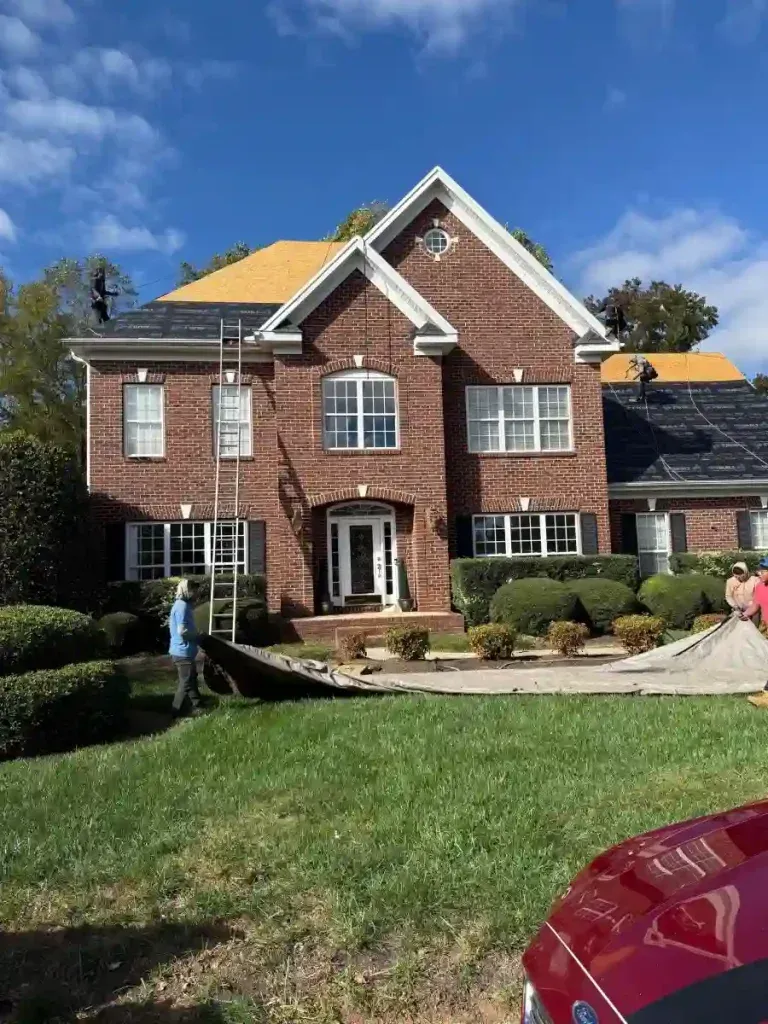 Roofers working on a brick house. Ladder propped against roof. Blue sky, green lawn.